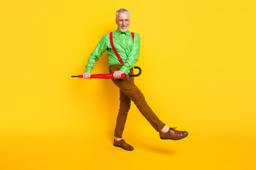 Full length profile side photo of senior man happy smile have fun go walk umbrella weather isolated over yellow color background