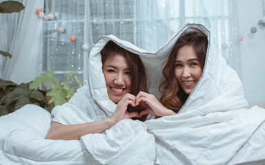 Two Asian beautiful adorable LGBT lesbian women lying down on bed, smiling with happiness and love...