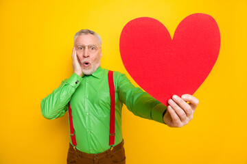 Photo portrait elder man amazed demonstrating red heart shaped postcard on date isolated vivid yellow color background