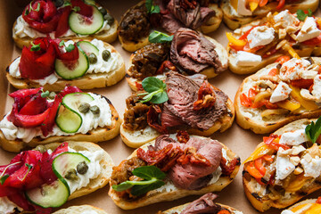 
A set of different snacks for a party or a festive table. Ciabatta sandwiches with tomatoes, jamon, cream cheese, vegetables, chambers and olives. Delicious wine snacks
