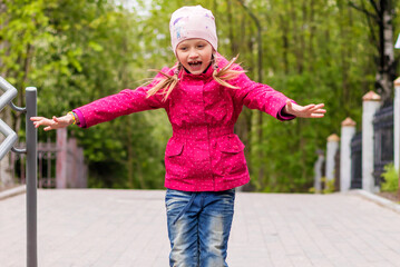 Cheerful happy girl on a walk in a jump with outstretched arms to the side.