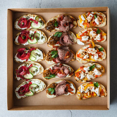 
A set of different snacks for a party or a festive table. Ciabatta sandwiches with tomatoes, jamon, cream cheese, vegetables, chambers and olives. Delicious wine snacks