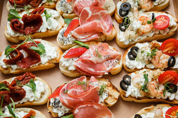 
A set of different snacks for a party or a festive table. Ciabatta sandwiches with tomatoes, jamon, cream cheese, vegetables, chambers and olives. Delicious wine snacks