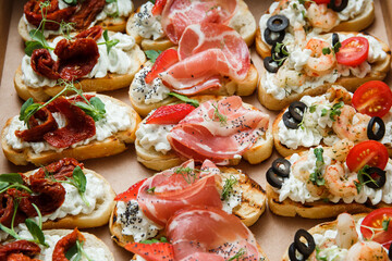 Fototapeta na wymiar A set of different snacks for a party or a festive table. Ciabatta sandwiches with tomatoes, jamon, cream cheese, vegetables, chambers and olives. Delicious wine snacks