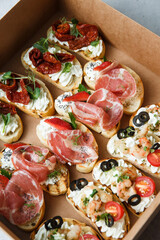 
A set of different snacks for a party or a festive table. Ciabatta sandwiches with tomatoes, jamon, cream cheese, vegetables, chambers and olives. Delicious wine snacks