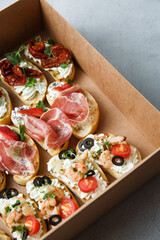 
A set of different snacks for a party or a festive table. Ciabatta sandwiches with tomatoes, jamon, cream cheese, vegetables, chambers and olives. Delicious wine snacks