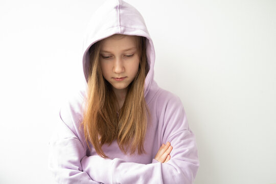 close up hooded upset girl with long hair in purple hoodie standing against white wall