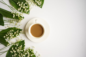 coffee with milk surrounded by lilies of the valley on a white background. free space