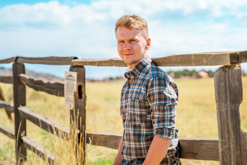 A young man stands near a wooden fence, a natural rustic landscape