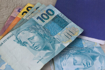 Brazilian money in paper and notebook on wooden surface.