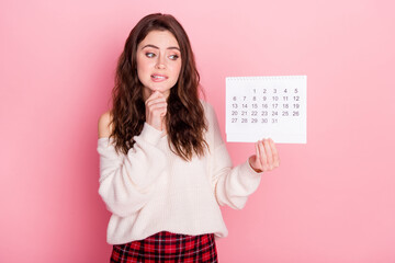Photo of guilty unsure young woman dressed white sweater biting lip holding calendar empty space...