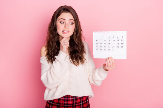 Photo of guilty unsure young woman dressed white sweater biting lip holding calendar empty space isolated pink color background