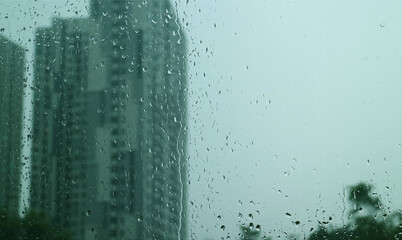 Closeup the texture of rain drops on window glass with blurry skyscrapers and overcast sky in background	