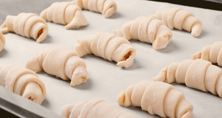 Fototapeta na wymiar Raw croissants with filling prepared to be baked on the parchment. Making bakery products at home