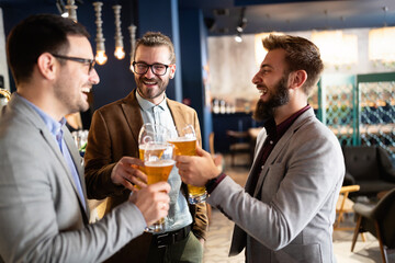 Leisure, friendship pub concept. Happy male friends drinking beer and clinking glasses at bar or pub