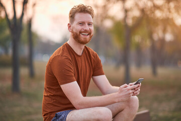 Young sporty man exercising in urban park and using modern smartphone.