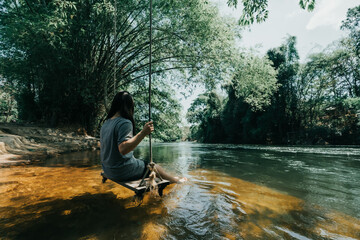 young cute Japanese hipster girl relaxing at beautiful lake view sitting river jungle mountains green forest at Phetchaburi, Kanchanaburi, Thailand. guiding idea women backpacker