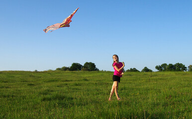Girl playing with flying kite on meadow.