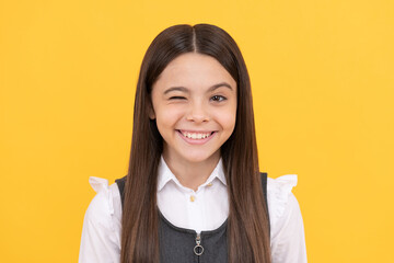 Happy school age girl child with smiling face give wink yellow background, winking