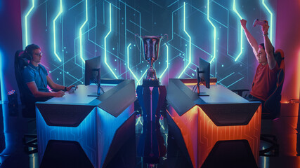 Two Professional Esport Gamers Using Controllers Playing Console Video Games on a Championship Event, One Player Celebrates Victory with Raised Hands. Global Online Streaming Cyber Gaming Tournament © Gorodenkoff
