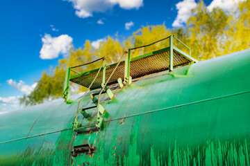 A close-up of an old railroad tank car with drips on board. A freight train is temporarily parked in the forest.