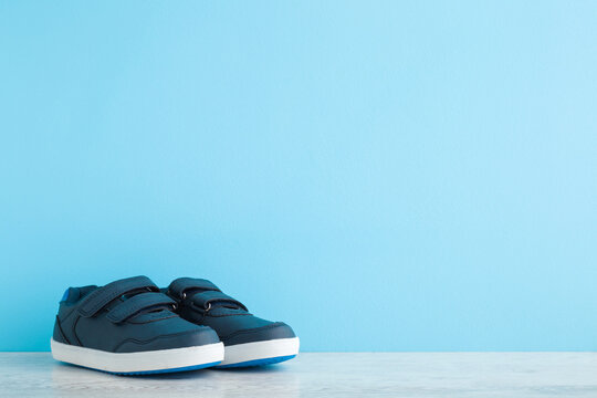 New Dark Sport Shoes For Little Kid On Wooden Floor At Light Blue Wall Background. Pastel Color. Baby Footwear. Closeup. Front View. Empty Place For Text.