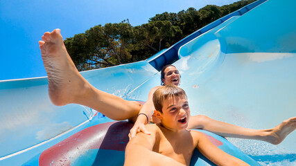 Happy cheerful caucasian son and mom laughing and shouting while sliding down fast on a water slide...
