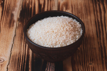 A brown clay bowl with round rice on a brown wooden table