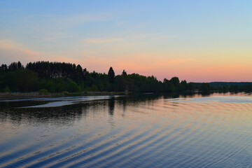 Early morning. Sunrise. View from the river with the reflection of the shore in the water and the wake of the ship.