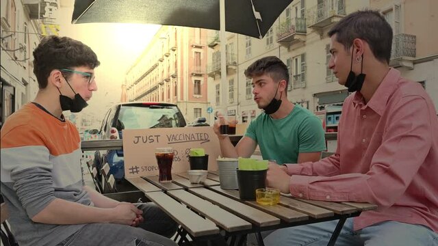 Three friends drink to celebrate the coronavirus vaccination. They have a sign saying stop covid, just vaccinated. Friends 1 covid 0. Concept of friendship, new normal, fight against pandemic.