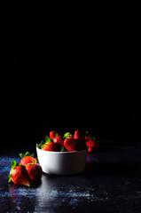 Bowl of ripe strawberries on blue background. Dark Food