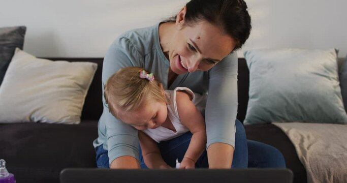 Caucasian mother with her baby smiling while using laptop at home