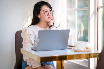 asian freelance Distracted from work worried people business female working with laptop computer with coffee cup and smartphone Pensive unmotivated looking at window in coffee shop like the background