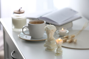 Fototapeta na wymiar Beautiful David bust candles and cup of hot drink on white table indoors, space for text