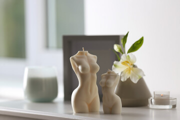 Beautiful body shaped candles and flower on white table indoors