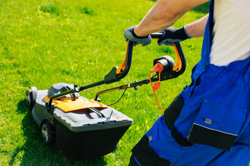 Young man mows the lawn using an electric lawn mower in a special worker suit near a large country...