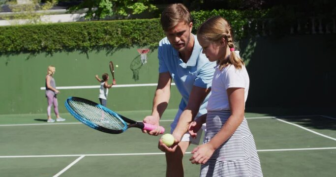 Caucasian father teaching his daughter to play tennis at tennis court on a bright sunny day