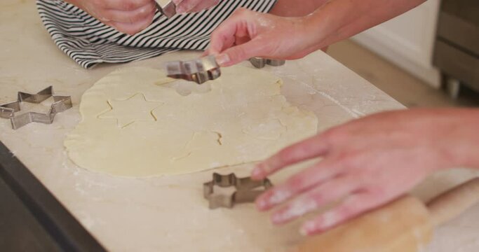 Mid section of mother and daughter cutting the dough with baking tin in star shapes in the kitchen