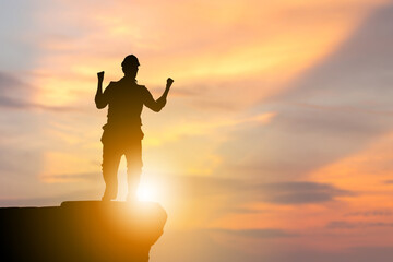 Fototapeta premium Silhouette of engineer man with clipping path celebrating victory on stone evening sky sunset background, success concepts