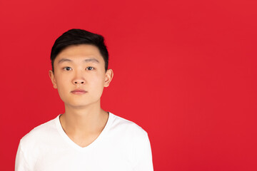 Asian young man's portrait on red studio background. Concept of human emotions, facial expression, youth, sales, ad.