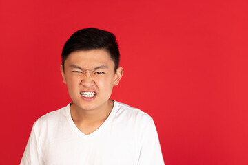 Asian young man's portrait on red studio background. Concept of human emotions, facial expression, youth, sales, ad.