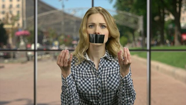 Angry woman with taped mouth looking at camera.