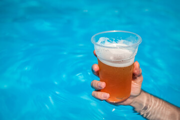 Close up of a man hand holding a pint of beer in swimming pool