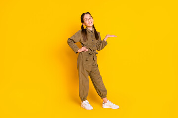Naklejka premium Full body portrait of cheerful pupil put arm on waist palm hold show empty space isolated on yellow color background