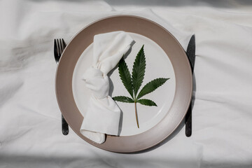 Cannabis friendly dinner concept. Beautiful dinner setup with marijuana leaves, knife and fork. Pastel colours. Copy space. 