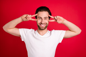 Photo of impressed youth brown hairdo man show v-sign wear white t-shirt isolated on vivid red color background