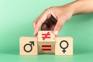 Hand flip wooden cube with symbol non-equality to equality with man and woman icons on green background