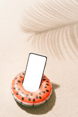 Inflatable watermelon shaped with a mobile phone inside on tropical beach sand with shadows of coconut tree leaves in summer. Travel and holiday concept background.vertical image with copy space © Zazú