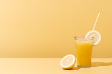 Refreshing glass of fruit juice with lemon and straw on a yellow background in a summer day.