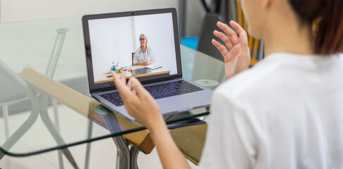 Obraz na płótnie Canvas Asian female patient having online video call with doctor on laptop. Young woman talking to medical practitioner consulting health specialist over internet. Online medical consultation concept.